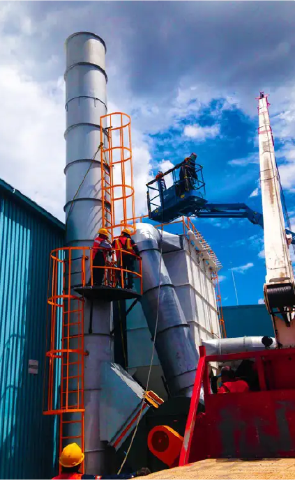 Técnicos instalando colector de polvo industrial con ductos verticales y chimenea metálica.
